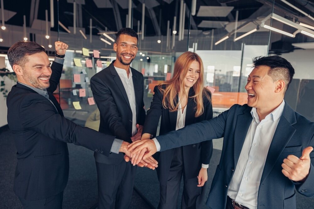 Enthusiastic members of the staffing company CTR Group celebrating in their successful acquisition of a new client for their bespoke staffing solutions, encapsulated in a unified group handshake and bright smiles, set against the backdrop of their sleek, modern office.